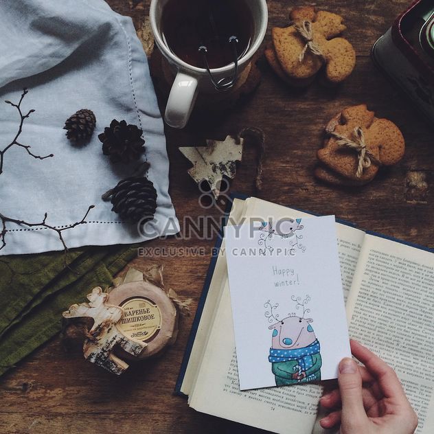 Cup of tea, cookies, open book and postcard in hand - бесплатный image #183803