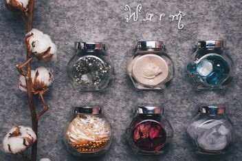 Small jars with decorations and branch of cotton on background - бесплатный image #342543