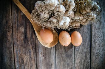 Garlic, eggs and wooden spoon on dark wooden background - бесплатный image #452403