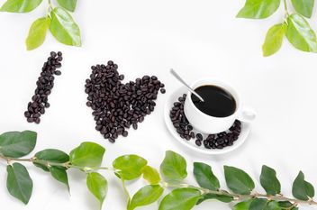 cup of coffee,coffee beans laid out in the shape of heart and green leaf on white background - бесплатный image #452573