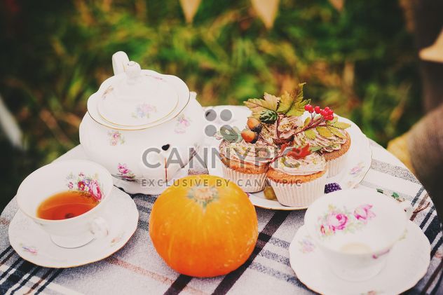 Tea in cups and teapot, cupcakes and pumpkin on the table - image #136203 gratis