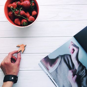 Strawberries in bowl, magazine and wooden bird in hand - бесплатный image #341343
