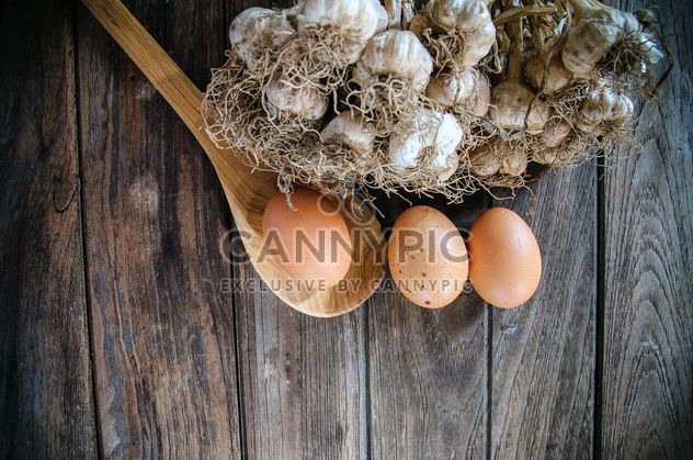 Garlic, eggs and wooden spoon on dark wooden background - бесплатный image #452403